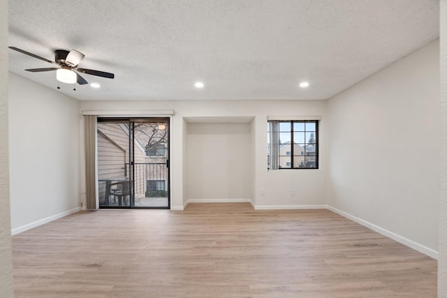 empty room featuring a wealth of natural light, light wood finished floors, baseboards, and a ceiling fan