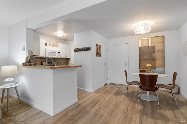 kitchen with white cabinetry, light hardwood / wood-style flooring, kitchen peninsula, and tasteful backsplash