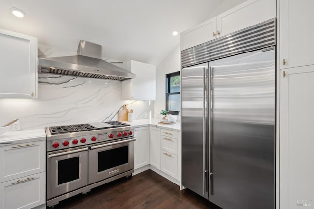 kitchen featuring high end appliances, white cabinetry, tasteful backsplash, vaulted ceiling, and range hood