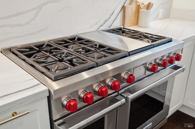 details with white cabinetry, double oven range, backsplash, and light stone counters