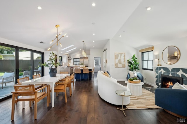 dining space featuring a tile fireplace, vaulted ceiling, dark wood-type flooring, and a notable chandelier