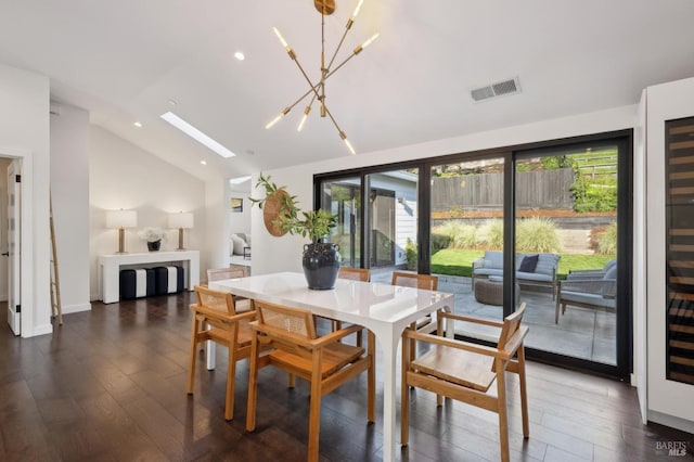 dining area with dark wood-type flooring, vaulted ceiling with skylight, and an inviting chandelier