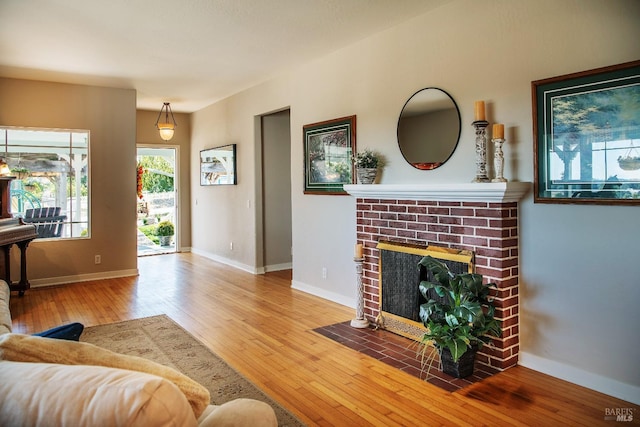 living room with baseboards, wood-type flooring, and a brick fireplace