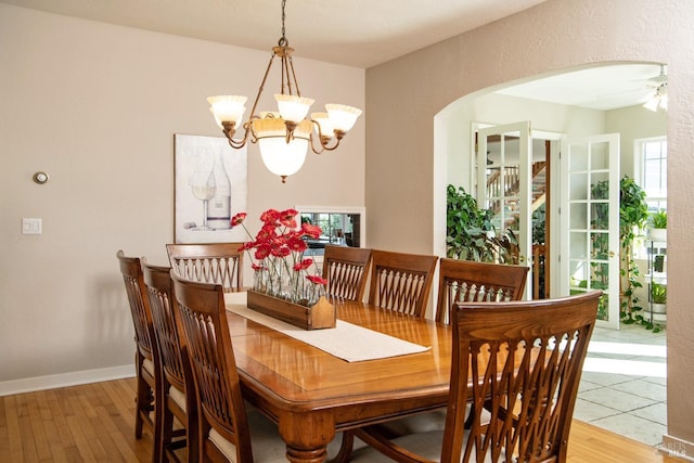 dining area with baseboards, arched walkways, wood finished floors, and ceiling fan with notable chandelier