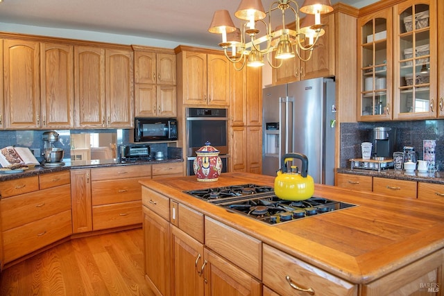 kitchen with light wood-style flooring, decorative backsplash, black appliances, glass insert cabinets, and butcher block counters