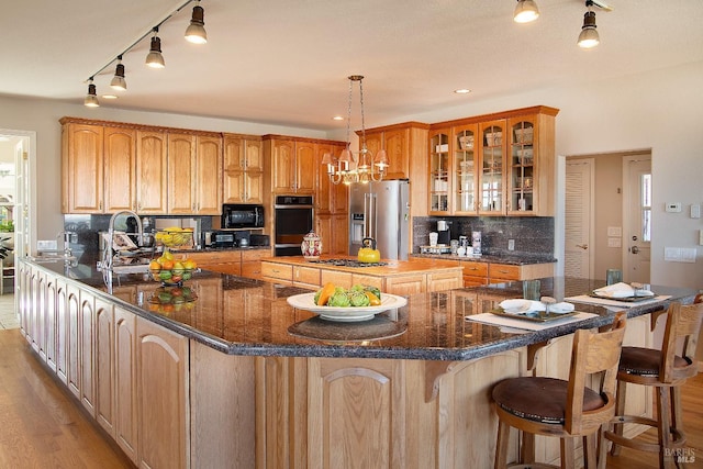 kitchen with backsplash, glass insert cabinets, light wood-style floors, a large island, and black appliances