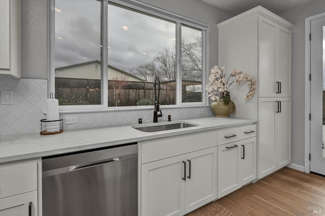 kitchen with sink, dishwasher, light stone countertops, light hardwood / wood-style floors, and white cabinets