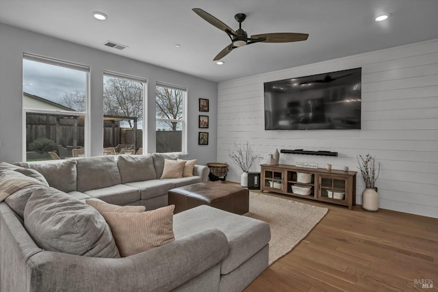 living room with hardwood / wood-style flooring, ceiling fan, and wood walls