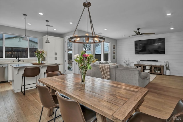 dining space featuring sink, light hardwood / wood-style floors, ceiling fan, and wood walls