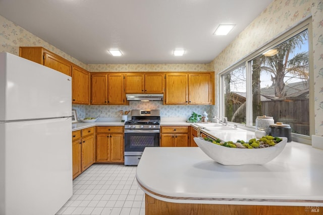 kitchen featuring sink, light tile patterned floors, stainless steel gas range oven, and white refrigerator