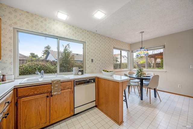 kitchen with pendant lighting, sink, dishwashing machine, kitchen peninsula, and a textured ceiling