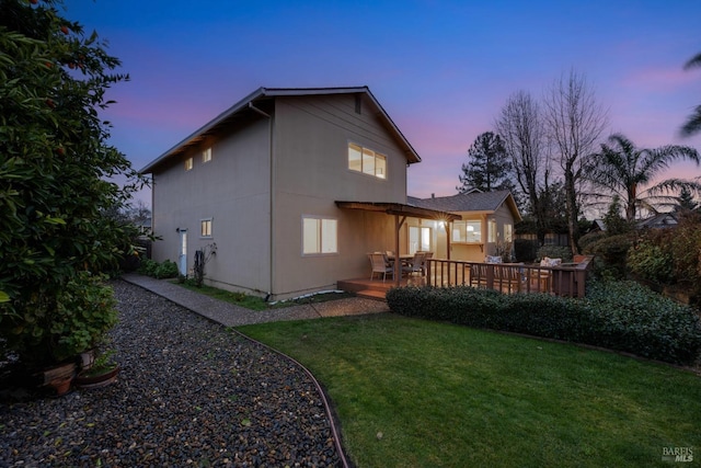 back house at dusk featuring a wooden deck, a yard, and a pergola