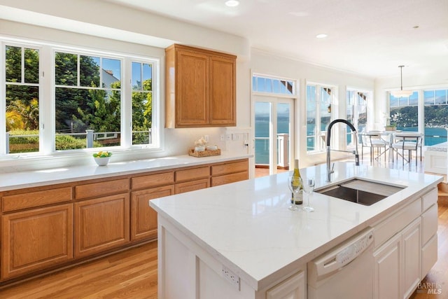 kitchen with light stone counters, a center island with sink, a water view, a sink, and dishwasher