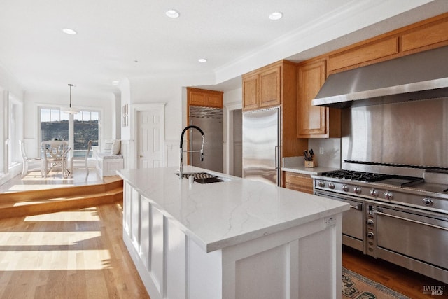 kitchen with light stone counters, a kitchen island with sink, hanging light fixtures, appliances with stainless steel finishes, and ventilation hood