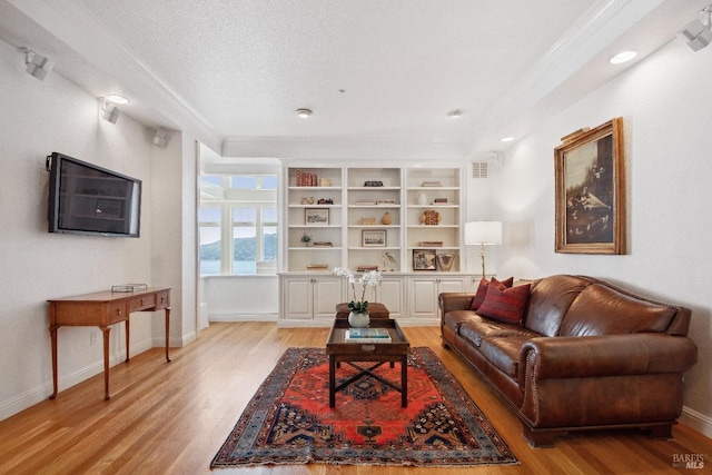 living area with light wood finished floors, baseboards, a textured ceiling, and ornamental molding