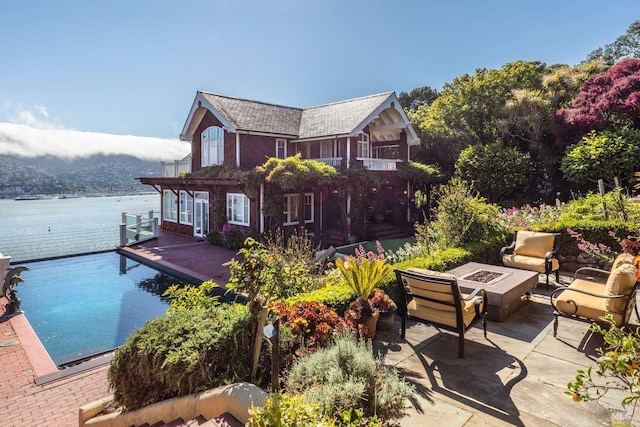 exterior space featuring a fire pit, a patio area, a water view, and a balcony