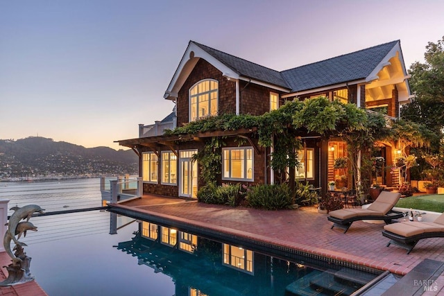 back house at dusk featuring a balcony, a mountain view, and a patio