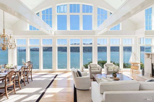 sunroom / solarium featuring vaulted ceiling, a water view, a fireplace, and an inviting chandelier