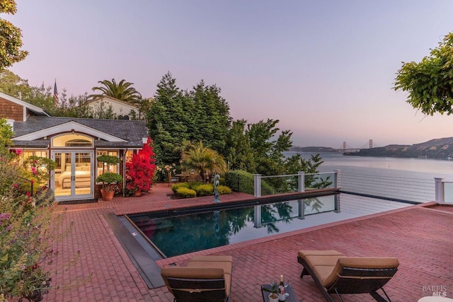 pool at dusk with a patio, a water view, and french doors