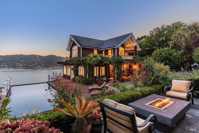 back of house at dusk featuring a patio area, a water view, a fire pit, and a balcony