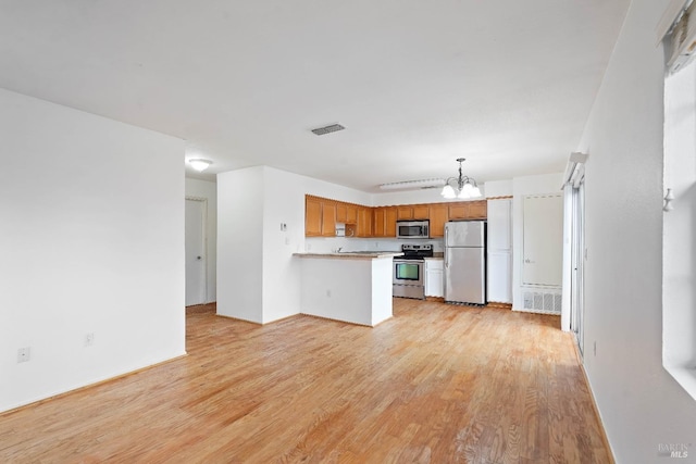 kitchen featuring appliances with stainless steel finishes, pendant lighting, a notable chandelier, and light wood-type flooring