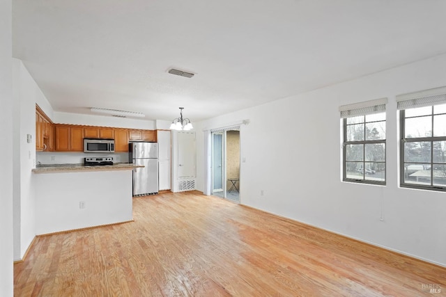 kitchen featuring hanging light fixtures, light hardwood / wood-style flooring, kitchen peninsula, a notable chandelier, and stainless steel appliances