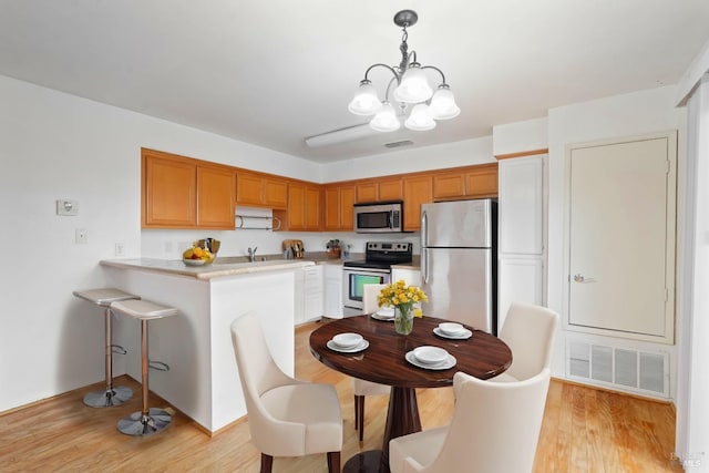 kitchen with decorative light fixtures, light wood-type flooring, kitchen peninsula, a notable chandelier, and stainless steel appliances