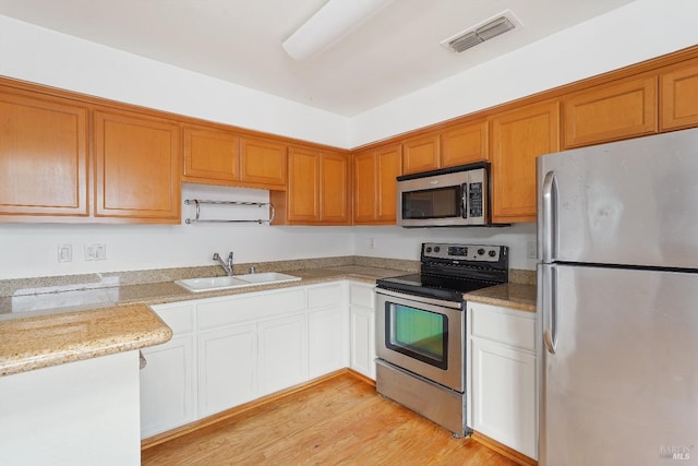 kitchen with sink, light stone counters, white cabinetry, light hardwood / wood-style flooring, and appliances with stainless steel finishes