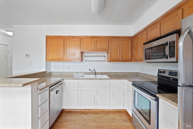 kitchen with sink, light stone counters, light wood-type flooring, kitchen peninsula, and stainless steel appliances