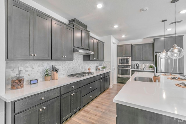 kitchen with sink, light hardwood / wood-style flooring, appliances with stainless steel finishes, tasteful backsplash, and decorative light fixtures