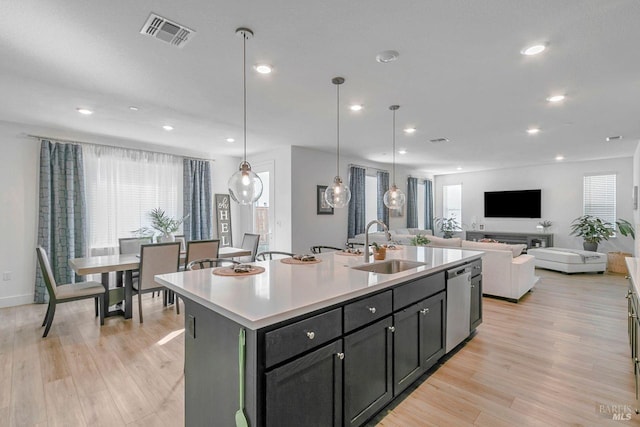 kitchen featuring sink, hanging light fixtures, dishwasher, an island with sink, and light hardwood / wood-style floors