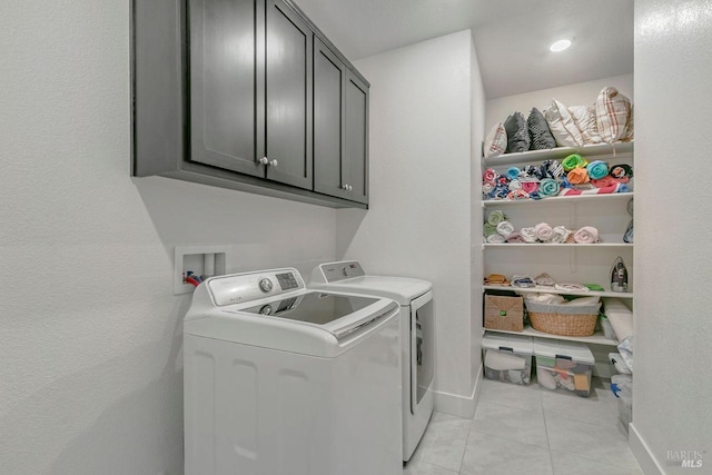 clothes washing area featuring light tile patterned floors, washing machine and dryer, and cabinets