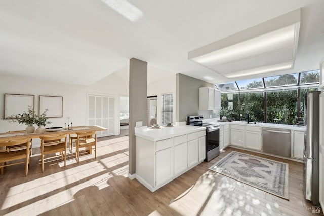 kitchen with appliances with stainless steel finishes, a wealth of natural light, white cabinets, and light hardwood / wood-style flooring