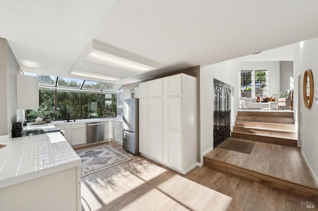 kitchen featuring white cabinetry, sink, light hardwood / wood-style floors, kitchen peninsula, and stainless steel appliances