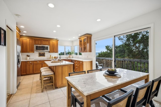 kitchen featuring a kitchen island, a breakfast bar, appliances with stainless steel finishes, light tile patterned floors, and light stone countertops