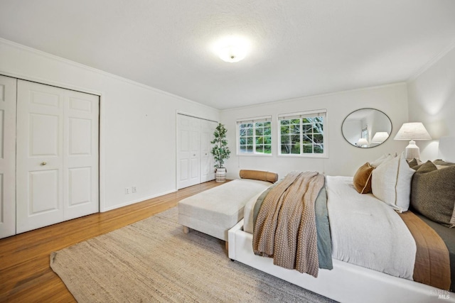 bedroom with multiple closets, crown molding, and hardwood / wood-style flooring