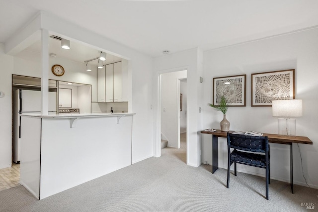 kitchen with a kitchen bar, light carpet, white refrigerator, kitchen peninsula, and white cabinets