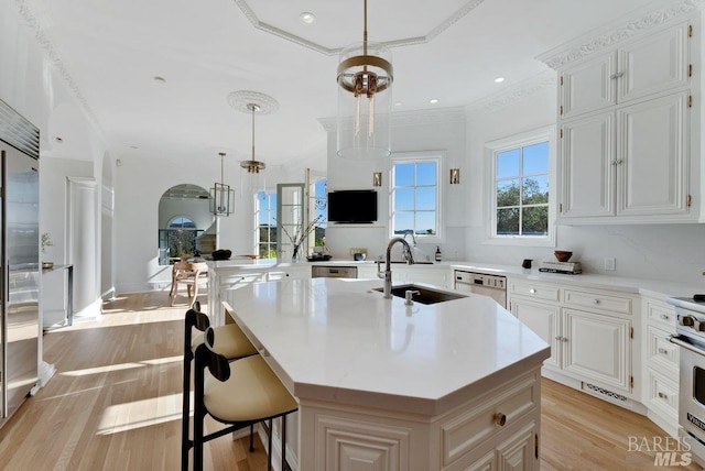 kitchen featuring hanging light fixtures, an island with sink, sink, and white cabinetry
