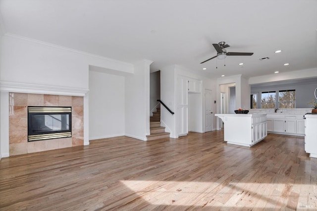 unfurnished living room with crown molding, a tile fireplace, ceiling fan, and light wood-type flooring