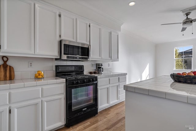 kitchen with black range with gas cooktop, white cabinetry, and tile counters