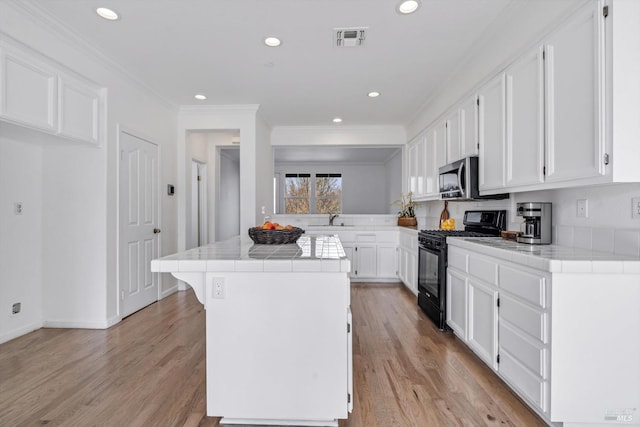 kitchen featuring sink, black range with gas cooktop, white cabinets, a kitchen island, and tile countertops