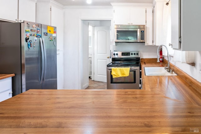 kitchen with sink, ornamental molding, white cabinets, and appliances with stainless steel finishes