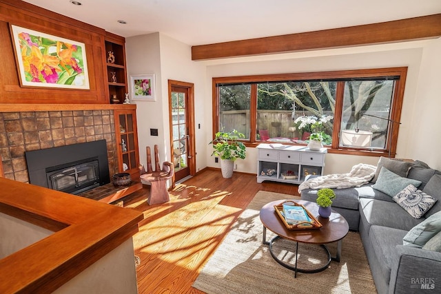 living room featuring built in features, baseboards, a tiled fireplace, and wood finished floors