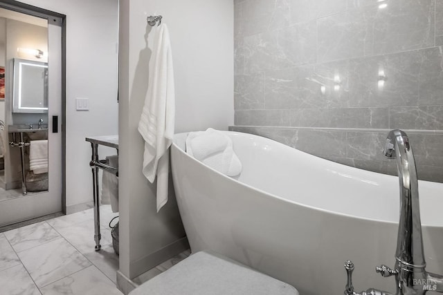 bathroom with marble finish floor and a freestanding tub