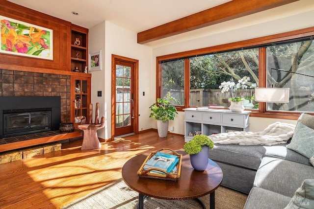 living room with a tiled fireplace, wood finished floors, beam ceiling, and baseboards