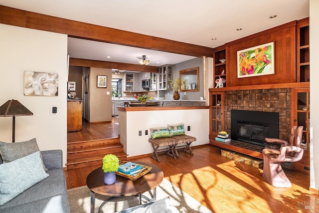 living room with built in shelves, a tile fireplace, wood finished floors, baseboards, and beam ceiling