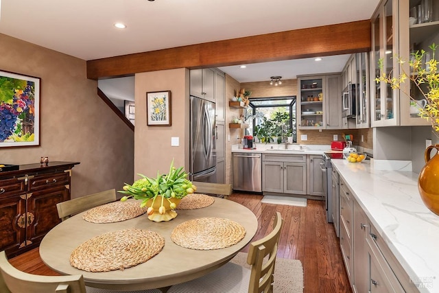 kitchen featuring appliances with stainless steel finishes, beamed ceiling, wood finished floors, gray cabinets, and a sink