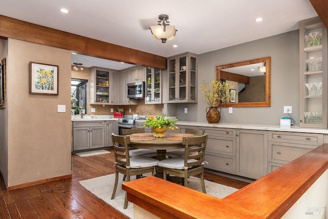 kitchen featuring dark wood finished floors, glass insert cabinets, appliances with stainless steel finishes, gray cabinetry, and recessed lighting