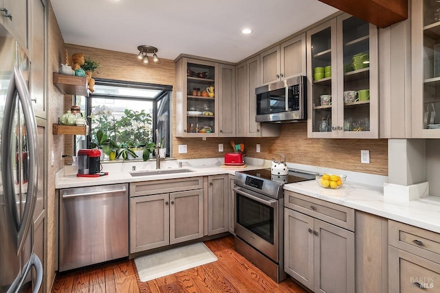 kitchen with stainless steel appliances, glass insert cabinets, a sink, and wood finished floors