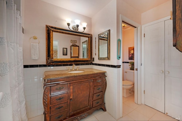 bathroom with toilet, vanity, tile walls, wainscoting, and tile patterned floors